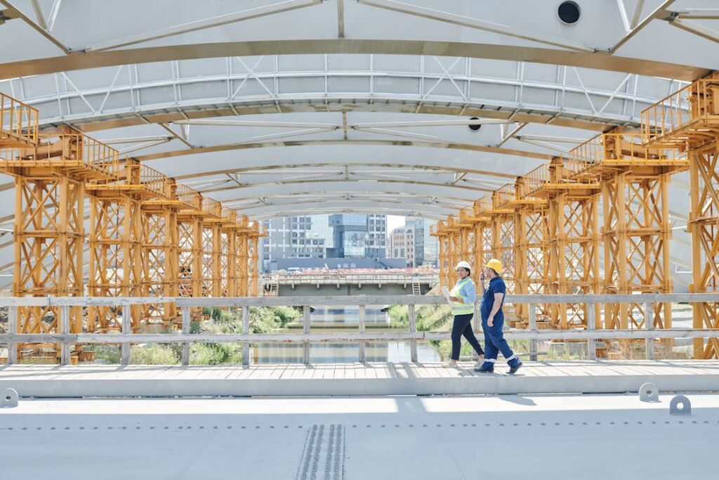 Two people walking over a bridge wearing construction attire.
