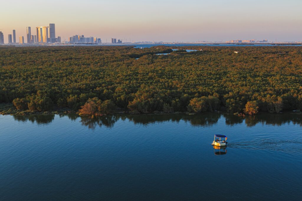 View of the Abu Dhabi city skyline with its skyscrapers with the sea canal and the eastern mangroves in the foreground. A tourboat is crossing the canal