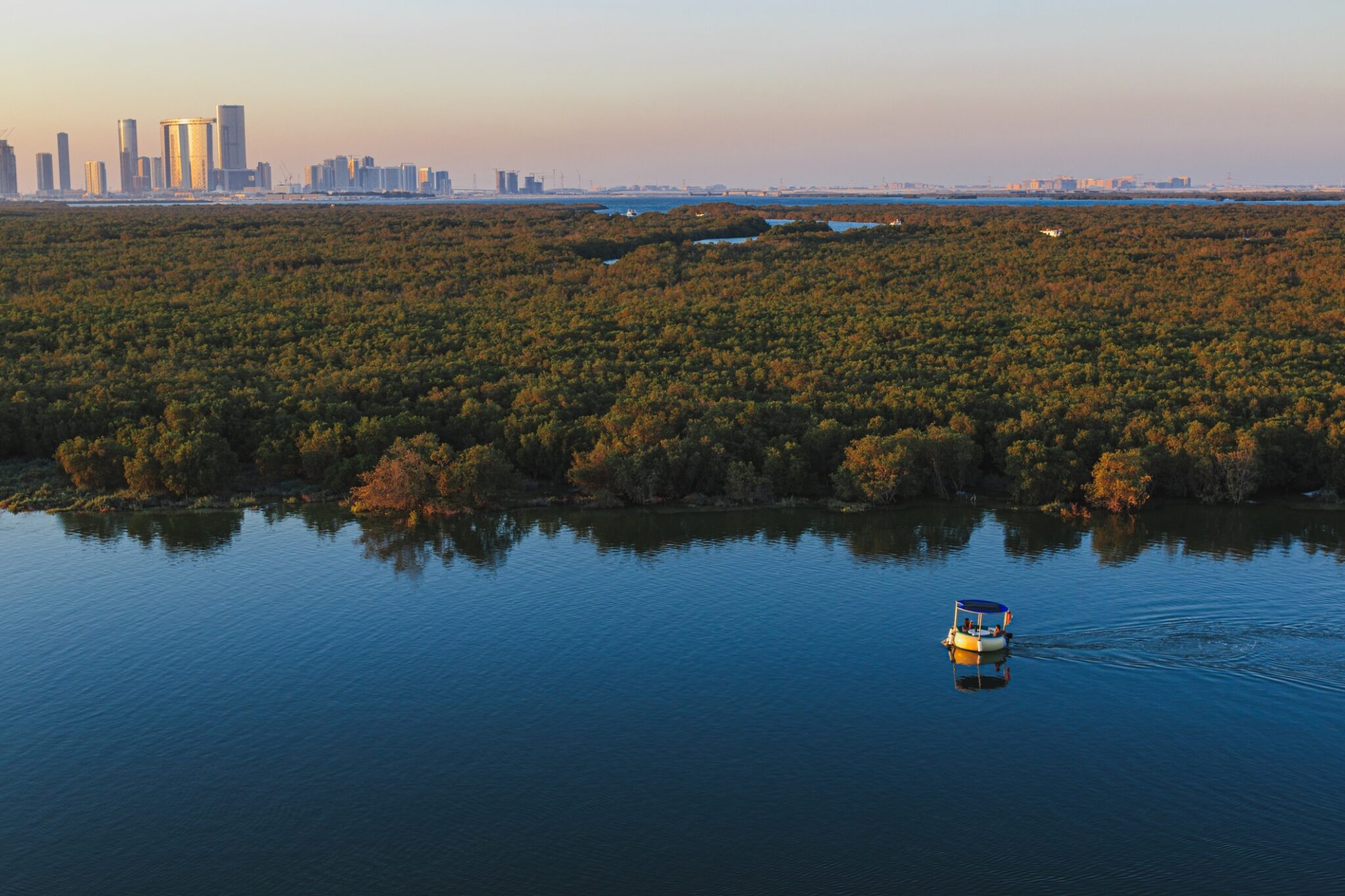 View of the Abu Dhabi city skyline with its skyscrapers with the sea canal and the eastern mangroves in the foreground. A tourboat is crossing the canal